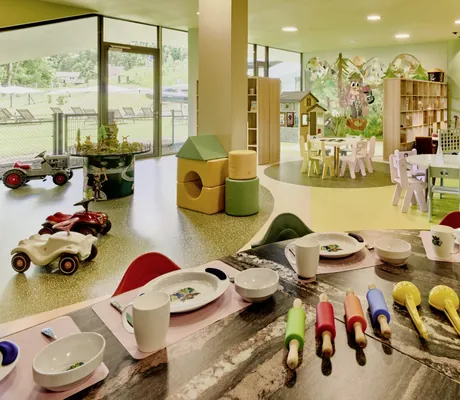 Bunter Spielbereich mit verschiedenen Spielzeugen, Tischen und Stühlen sowie großen Fenstern mit Blick nach draußen im Falkensteiner Family Hotel Montafon