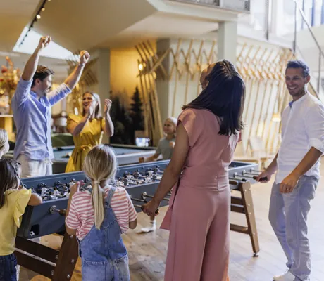 Kinder und Erwachsene spielen begeistert Tischkicker im modernen Lobbybereich des Falkensteiner Family Hotel Montafon