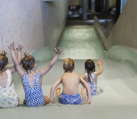 Vier Kinder in Badekleidung rutschen eine Wasserrutsche hinunter im Falkensteiner Family Hotel Montafon