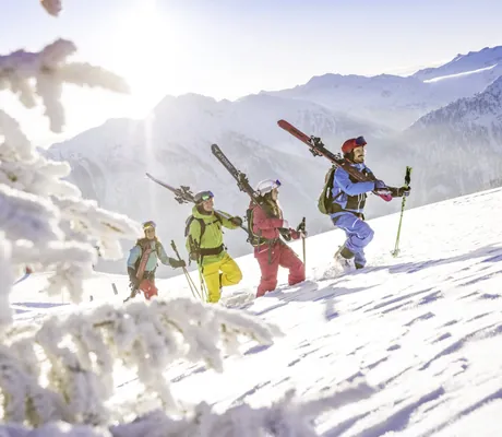 Eine Gruppe Skifahrer trägt die Skier den schneebhangenen Berg in der Sonnberg Ferienanlage herauf.