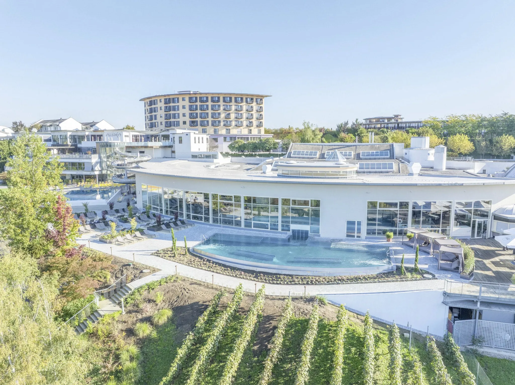 Outdoorpool vor der Hotelfassade des Allegria Resort Stegersbach hinter Weingärten
