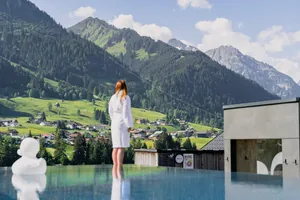 Frau in weißem Bademantel steht am Outdoorpool des Genuss- und Aktivhotel Sonnenburg, bewaldetete Berge im Hintergrund