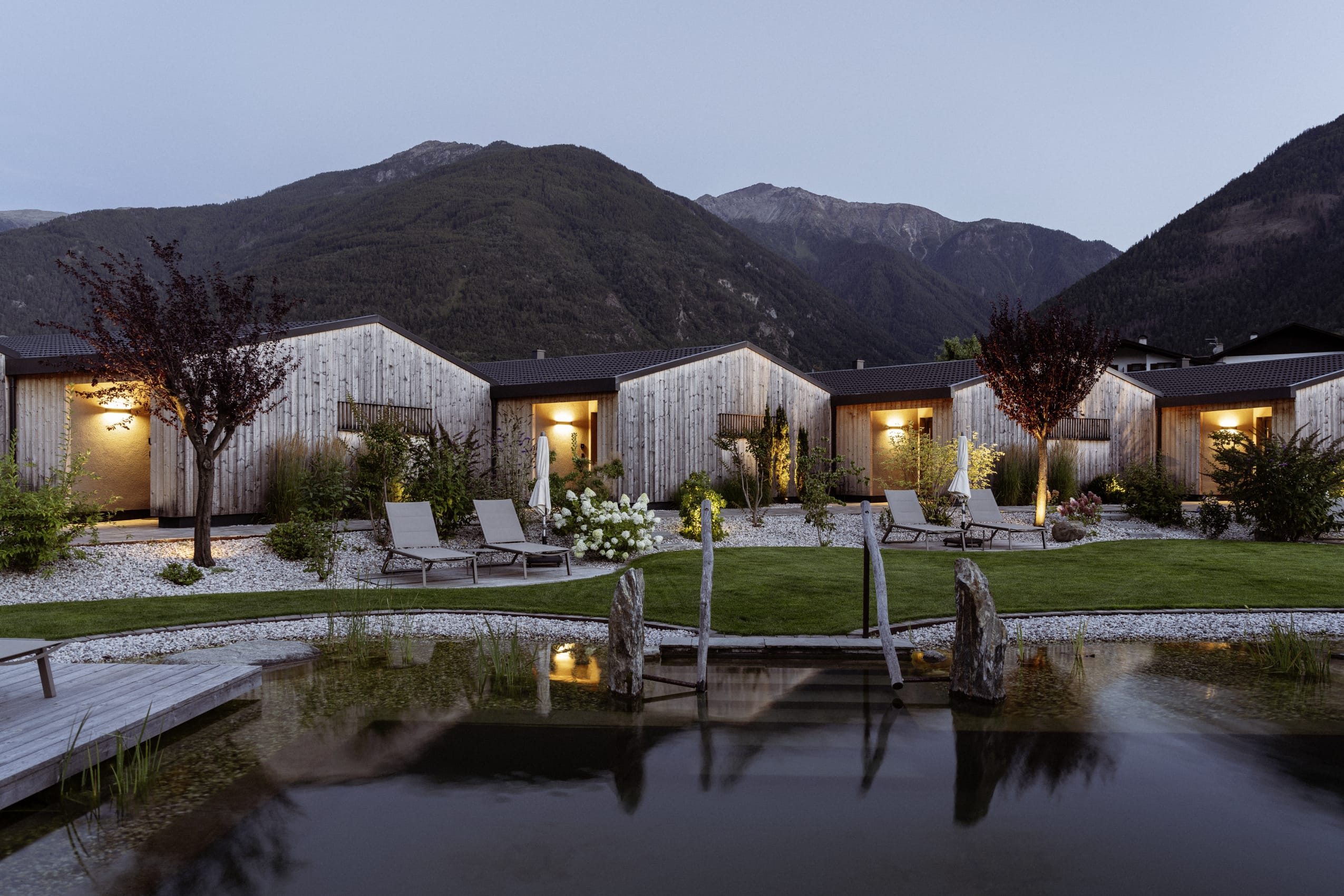 Das Amolaris Garden Lodge & Guesthouse in Goldrain bei Dämmerung mit See und Bergwelt im Hintergrund.