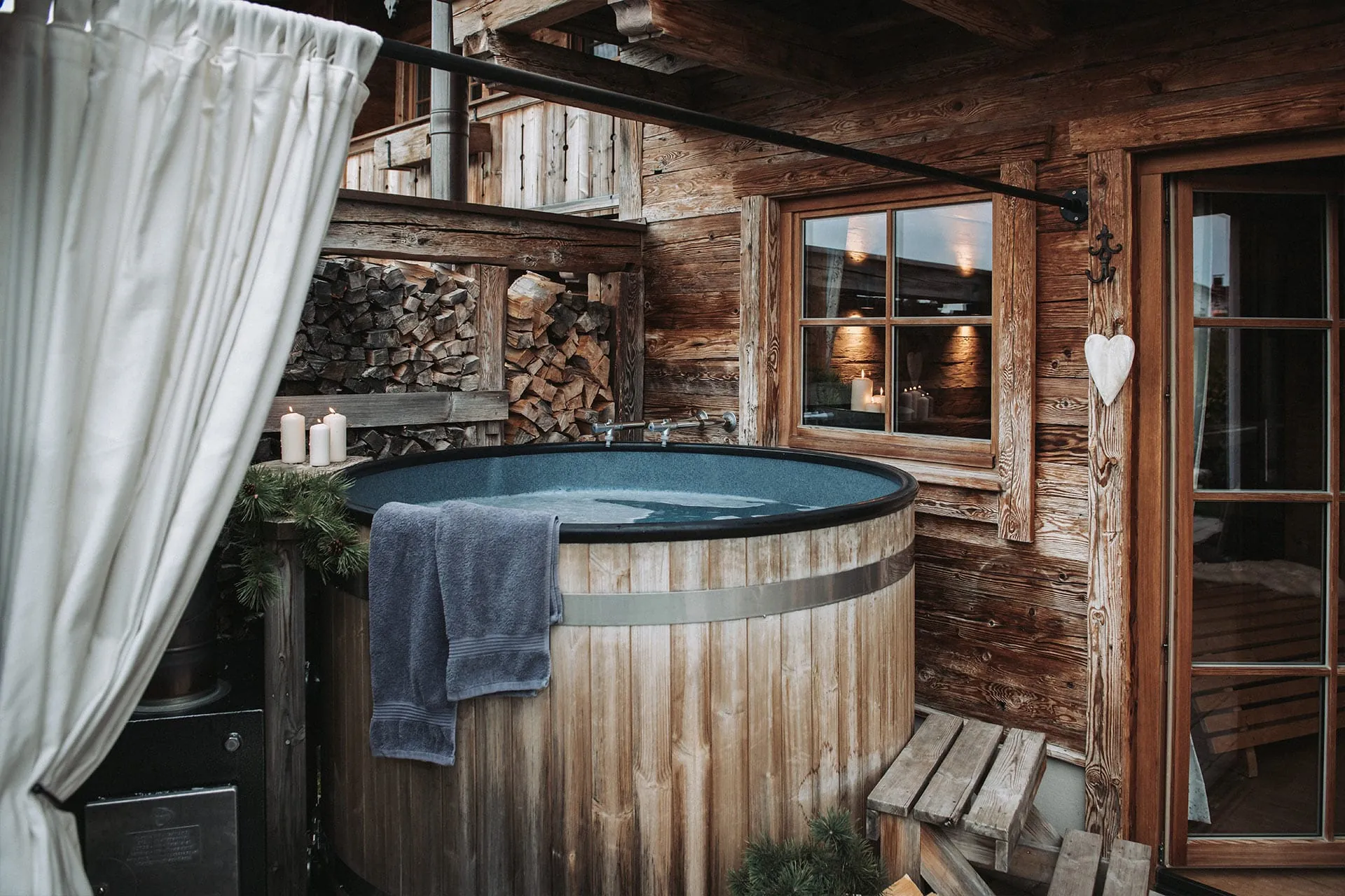 Außenansicht eines rustikalen Holz-Badezubers der Alpzitt-Chalets mit Kerzen