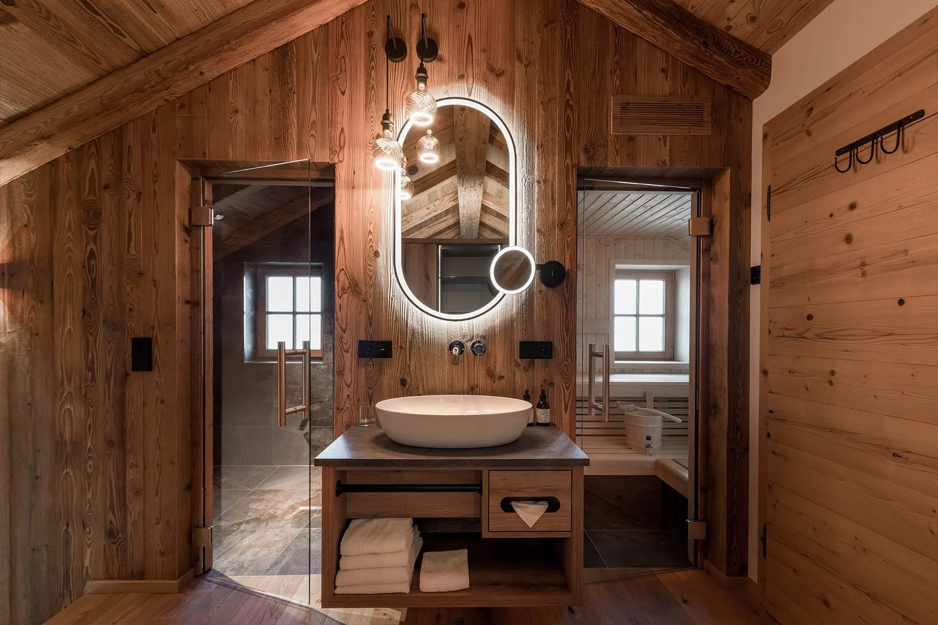 Stilvoller Chalet-Badezimmerbereich in den Alpzitt-Chalets mit beleuchtetem Spiegel, moderner Sauna und Holzinterieur