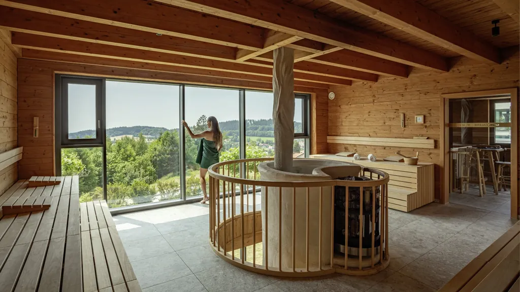 Eine Frau in der Sauna im Angerhof Sport- & Wellnesshotel mit bodentiefen Panoramafenstern und Blick ins Gr&uuml;ne.