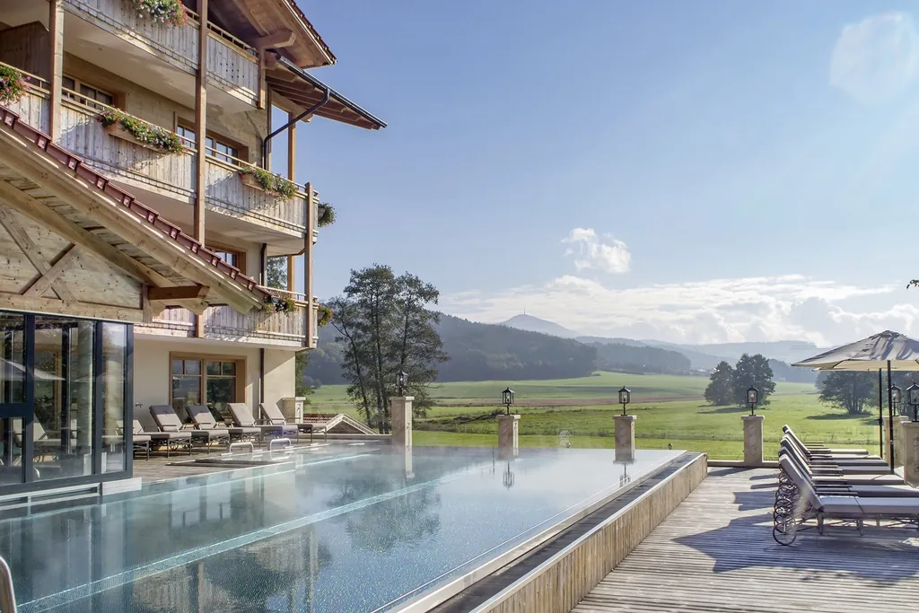 Die Hotelfassade mit Au&szlig;enpool des Hotel Brunner Hof in Arnschwang mit Bergpanorama.