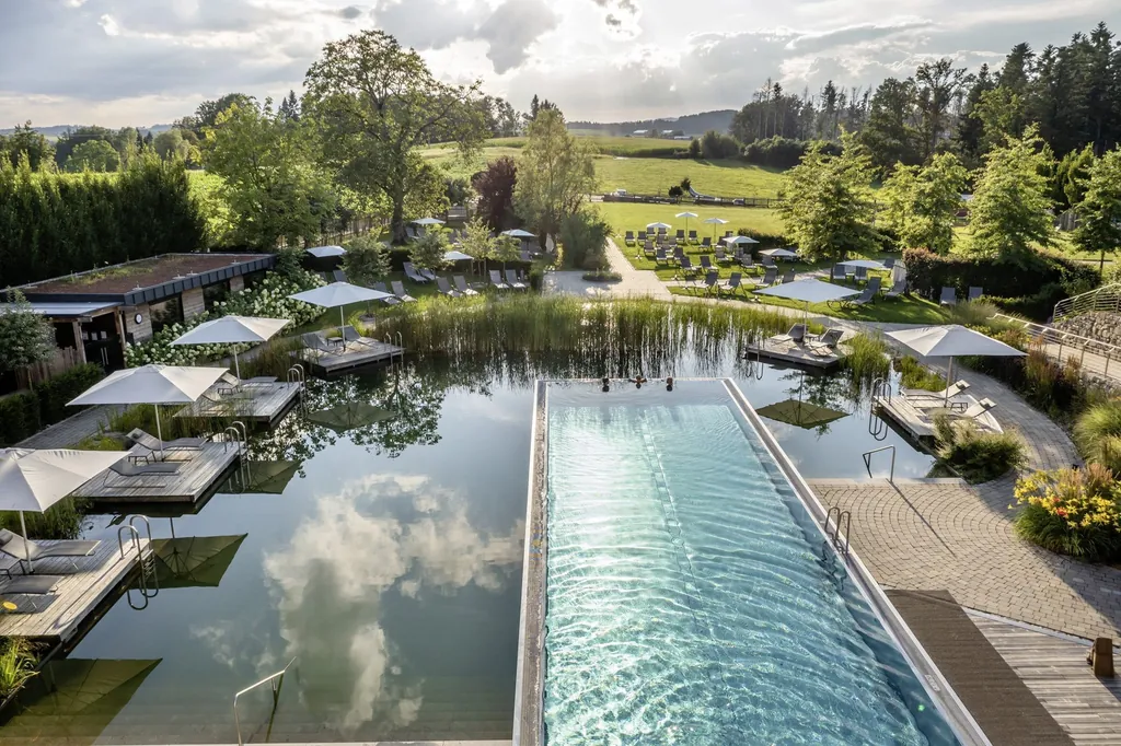 Der Au&szlig;enbereich im Wellnesshotel DAS STEMP mit Naturbadesee und Infinitypool mit Blick in die gr&uuml;ne Landschaft.