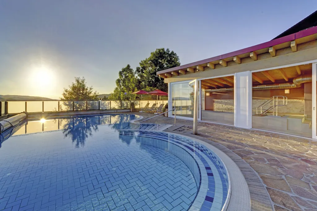 Der Outdoorpool im Wellnesshotel Hofbr&auml;uhaus bei sinkender Sonne mit Hotelfassade und Blick in die Landschaft des Bayerischen Waldes.