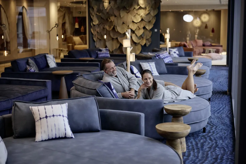 Ein Paar in Badem&auml;nteln liegt im Ruhebereich auf blauen Day Beds im Hotel Holzapfel.