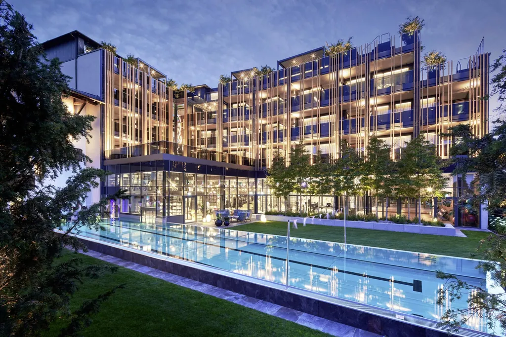 Au&szlig;enbereich mit weitl&auml;ufigem Schwimmbecken und beleuchteter Fassade des Wellnesshotel Jagdhof in der Abendd&auml;mmerung.