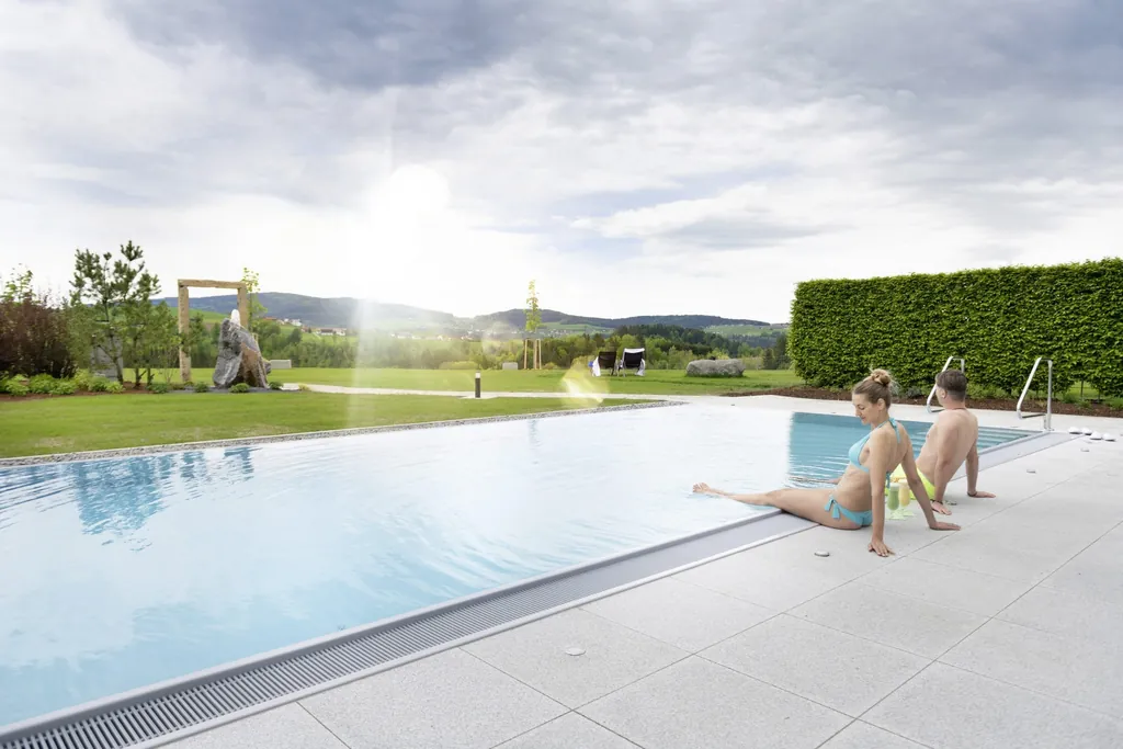 Paar sitzt am Infinitypool im Au&szlig;enbereich im Landrefugium Oberm&uuml;ller in Untergriessbach und genie&szlig;t die gr&uuml;ne Landschaft und W&auml;rme des Pools.