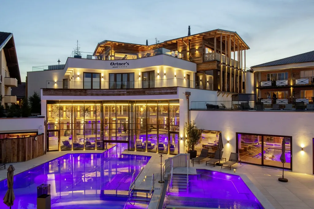 Die Au&szlig;enansicht des Hotels Ortners Resort in Bad F&uuml;ssing mit goldenen Lichtelementen und Outdoorpool.