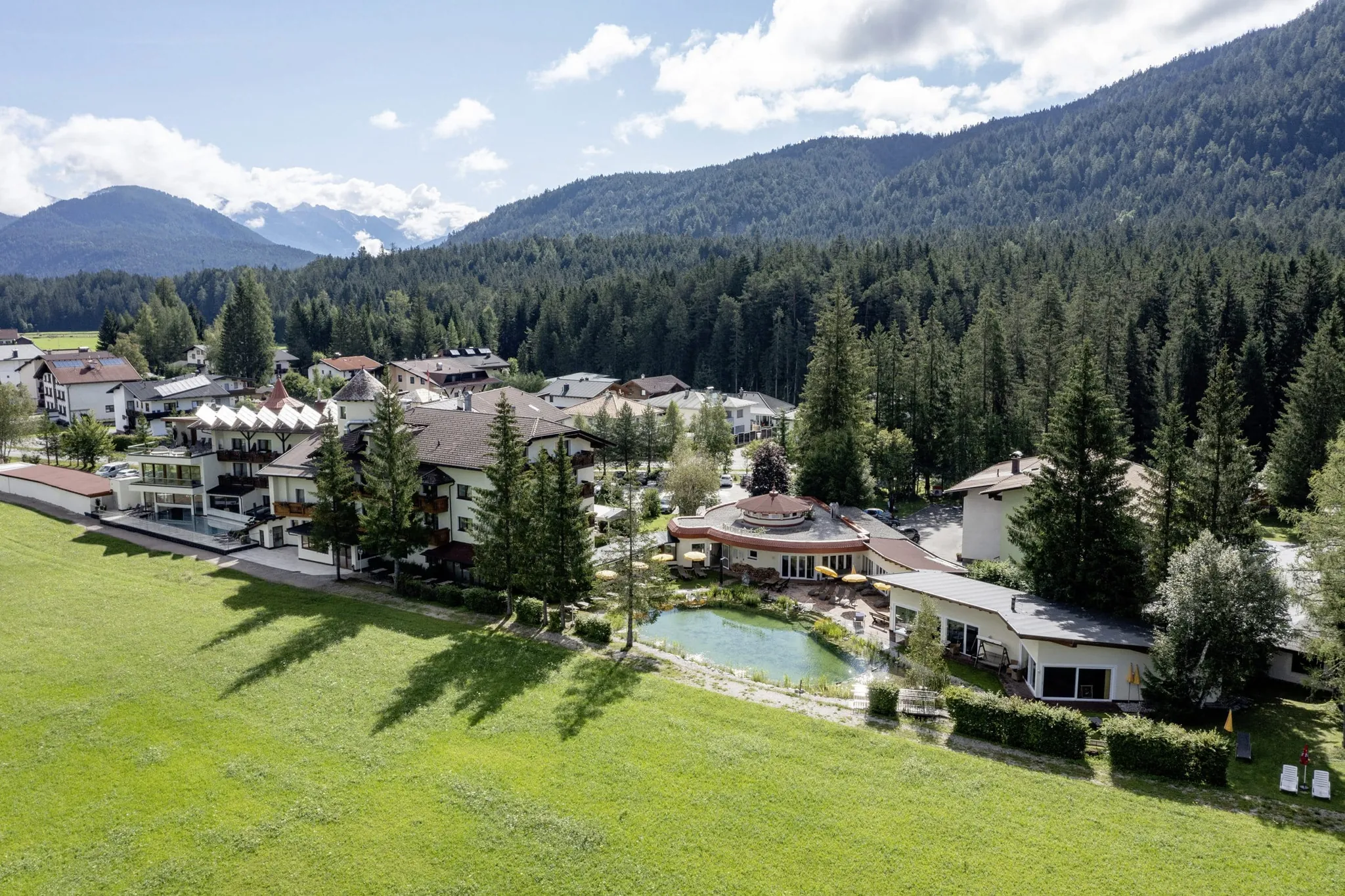 Drohnenansicht des Alpenhotel Karwendel mit Naturteich und Blick auf die bewaldeten Berge