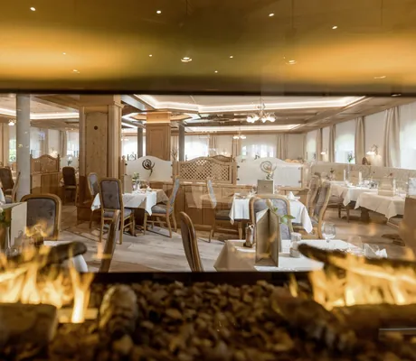 loderndes Kaminfeuer im rustikalen Restaurant des Alpenhotel Karwendel mit eingedeckten Tischen
