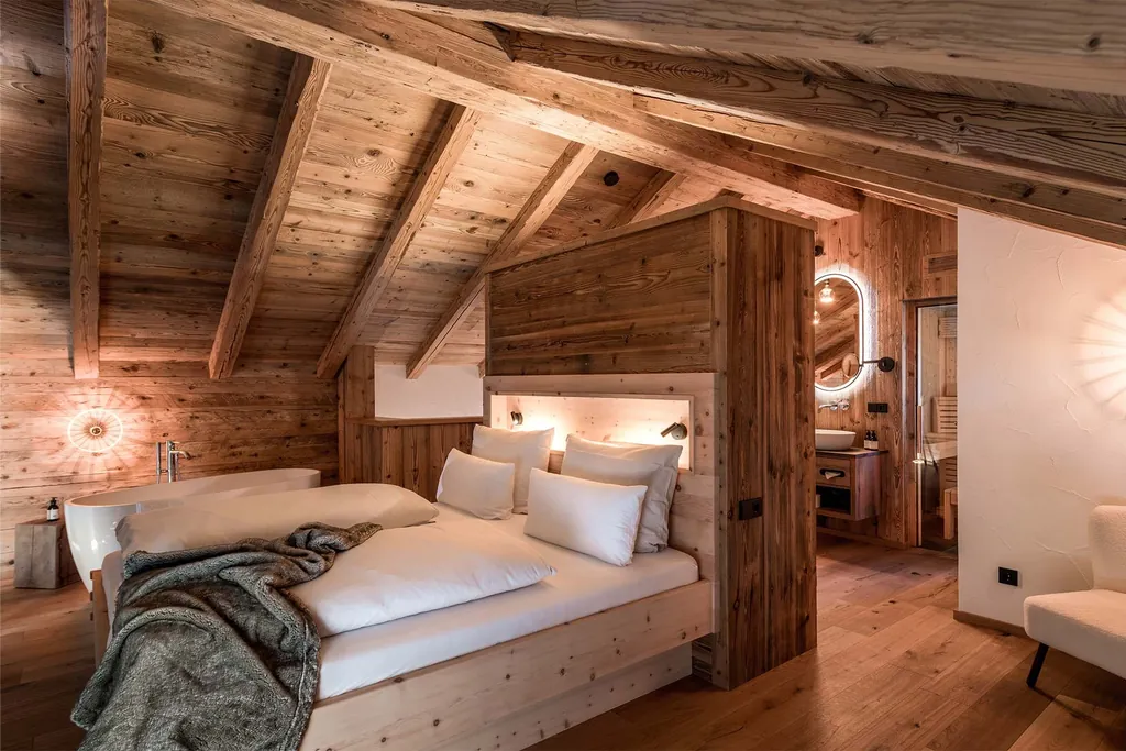 Doppelbett in einem der Alpzitt-Chalets mit Holzwänden, freistehender Badewanne und stimmungsvoller Beleuchtung