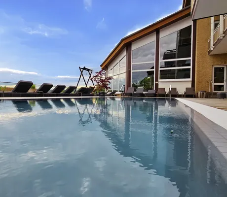 Outdoorpool des Göbels Hotel Rodenberg mit angrenzender Fassade und dunklen Liegen