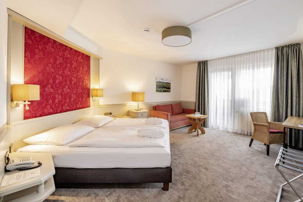 Doppelzimmer in Göbels Hotel Rodenberg mit roter Tapete hinter dem Bettkopf und gestreiftem Sofa