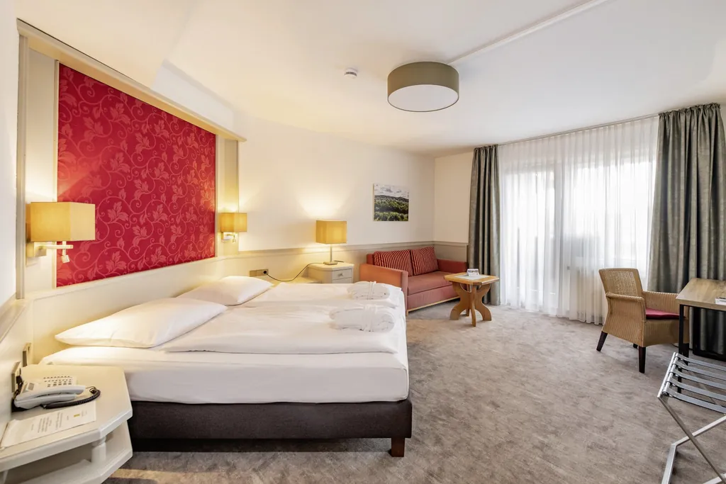 Doppelzimmer in Göbels Hotel Rodenberg mit roter Tapete hinter dem Bettkopf und gestreiftem Sofa