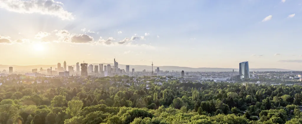 Panoramablick auf die Skyline von Frankfurt am Main bei Sonnenuntergang, umgeben von grünen Wäldern und Landschaften