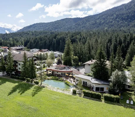 Drohnenansicht des Alpenhotel Karwendel mit Naturteich und Blick auf die bewaldeten Berge