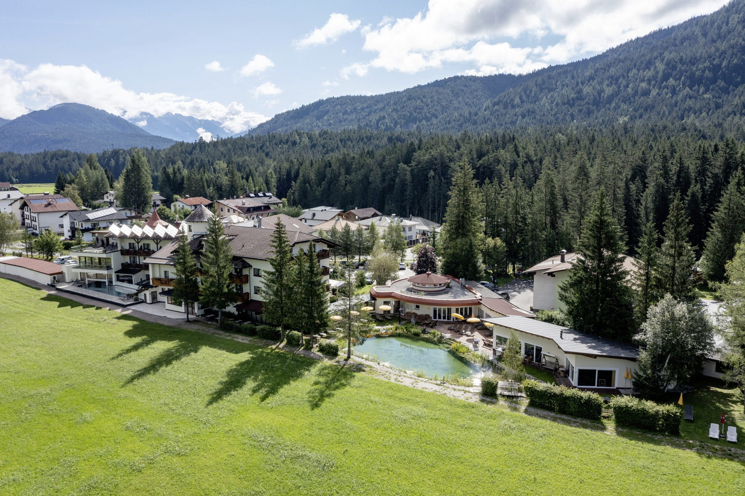 Drohnenansicht des Alpenhotel Karwendel mit Naturteich und Blick auf die bewaldeten Berge