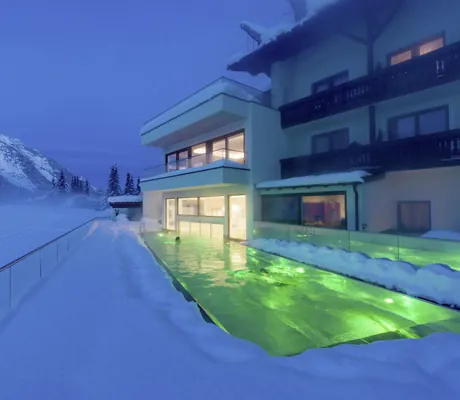 grün beleuchteter Outdoorpool im Alpenhotel Karwendel imm tiefen Schnee