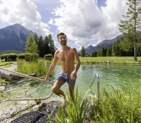 Mann in Badehose steigt aus dem Naturteich des Alpenhotel Karwendel