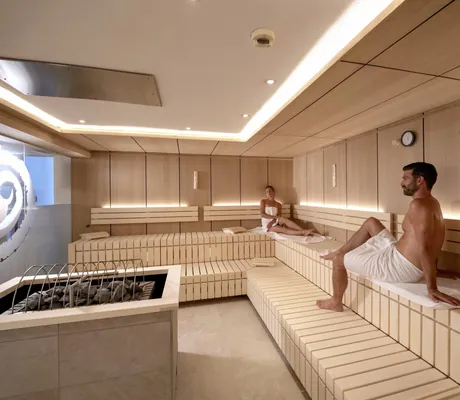 Paar in weißen Handtüchern sitzt in der Sauna des Alpenhotel Karwendel mit Ornament an der Glastür