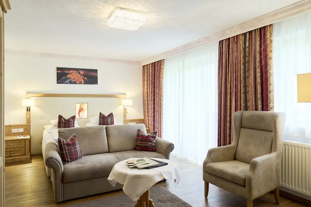 Zimmer im alpenländischen Stil im Alpenhotel Karwendel mit roten Brokatvorhängen und beigem Ohrensessel