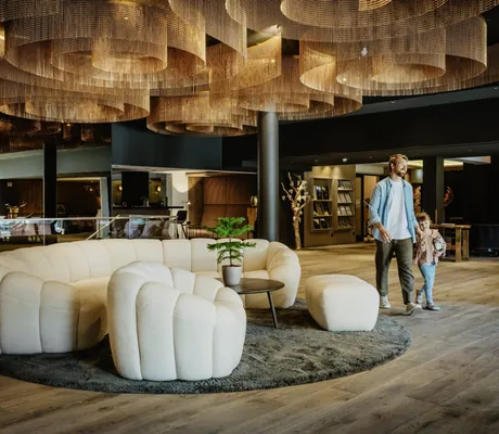 Mann geht mit kleinem Mädchen durch die Lobby des Bodenmaiser Hof mit weißem Sofaelement und goldenen Deckenornamenten