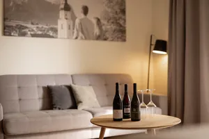 Gemütliches Wohnzimmer im Das Parkhotel mit grauem Sofa, Holztisch, drei Weinflaschen, Gläsern und einer Stehlampe in warmem Licht