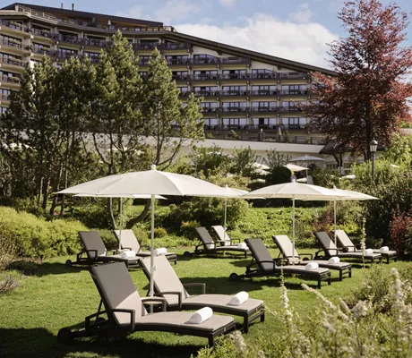 Sonnenschirme und Liegen im grünen Garten des Interalpen-Hotel Tyrol mit Hotelfassade im Hintergrund