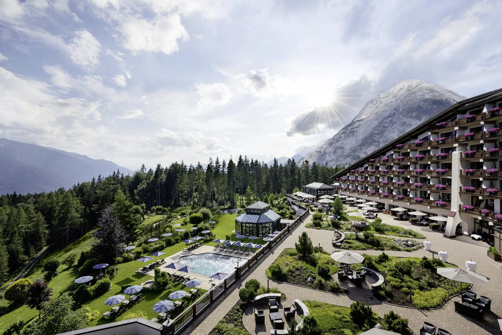 Sommerliche Außenansicht des Wellnesshotels Interalpen-Hotel Tyrol mit Garten, Pool und Bergkulisse im Hintergrund