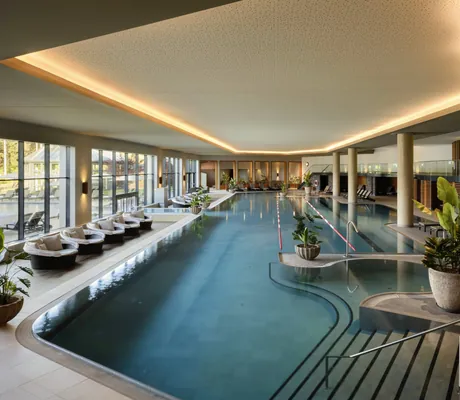 Moderner Indoorpool im Interalpen-Hotel Tyrol mit Liegebereichen und großen Fensterfronten, umgeben von Pflanzen