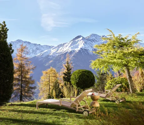 Zwei Liegen auf einer grünen Wiese des Interalpen-Hotel Tyrol mit Blick auf die herbstliche Berglandschaft und schneebedeckte Alpen