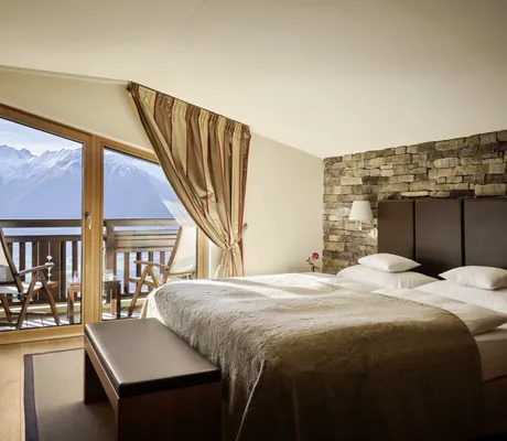 Premium-Zimmer im Interalpen-Hotel Tyrol mit Doppelbett, Steinwand, Balkon und Alpenblick durch große Fenster
