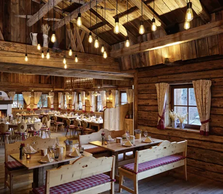 Rustikale Alm des Interalpen-Hotel Tyrol mit Holzinterieur, Kamin und warmem Licht für gemütliche Atmosphäre