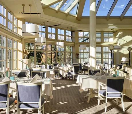 Heller Wintergarten des Restaurants im Interalpen-Hotel Tyrol mit gedeckten Tischen, großen Fensterfronten und Panoramablick auf die Berge