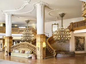 Elegante Hotellobby im Interalpen-Hotel Tyrol mit kunstvoller Holztreppe, prächtigen Kronleuchtern und detailreichen Stuckarbeiten