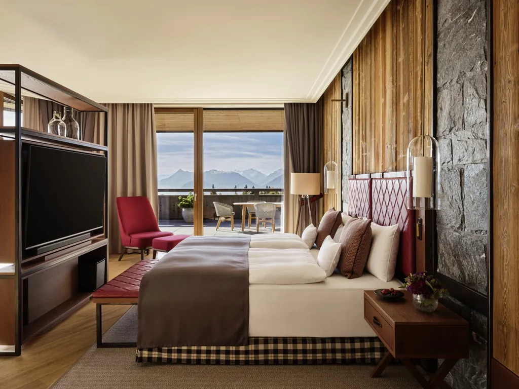 Luxuriöses Schlafzimmer einer Suite im Interalpen-Hotel Tyrol mit Doppelbett, Holz- und Steinakzenten sowie Balkon mit Alpenpanorama