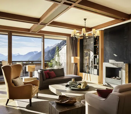 Stilvoller Wohnbereich einer Suite im Interalpen-Hotel Tyrol mit Kamin, Designmöbeln und Panoramafenster mit Bergblick