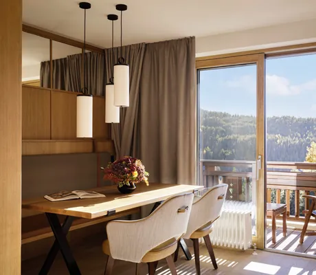 Gemütlicher Essbereich mit Holztisch, modernen Lampen und Balkon mit Blick auf die umliegende Natur im Interalpen-Hotel Tyrol