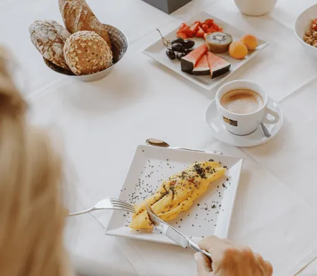 Eine Frau schneidet ein hausgemachtes Omelette beim Frühstück im Wellnesshotel My Paradies an.
