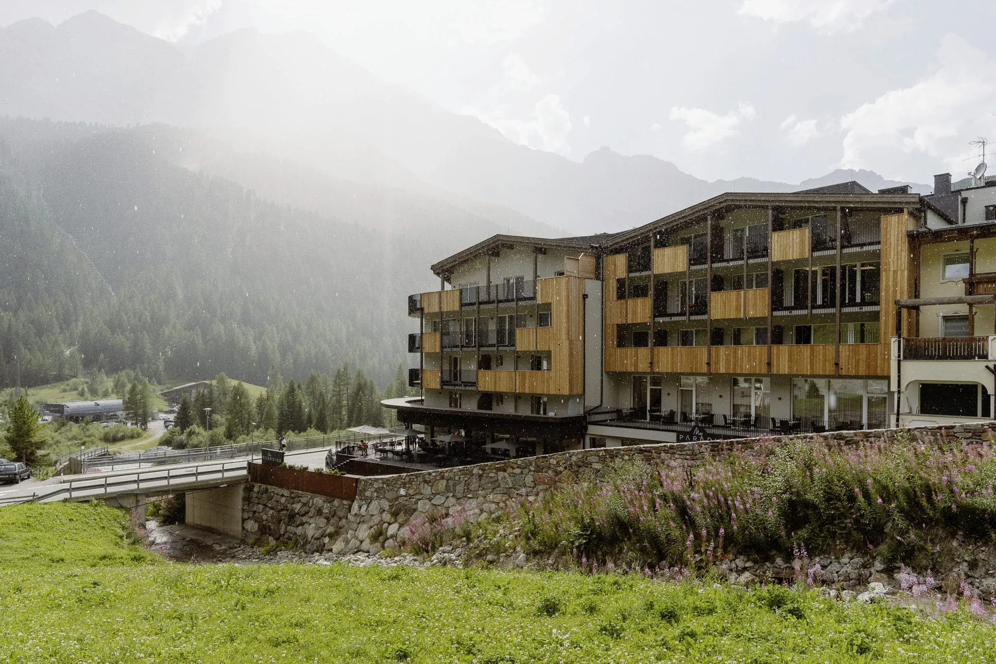 Außenfassade des Wellnesshotels My Paradies in Sulden mit strahlendem Sonnenschein und Wald.