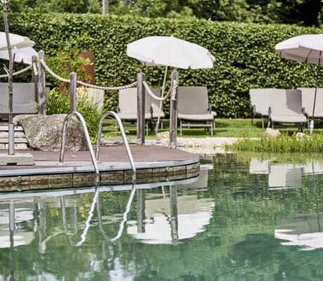 Holzponton am Naturbadeteich im Wellnesshotel Zum Bräu mit weißen Sonnenschirmen und Absperr-Kordel
