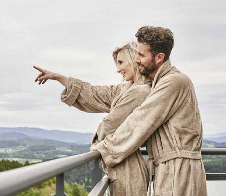 Paar in braunen Bademänteln steht auf dem Balkon des Wellnesshotel Zum Bräu und schaut in die Ferne