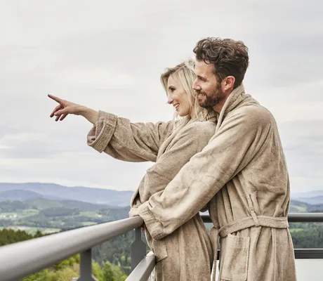 Paar in braunen Bademänteln steht auf dem Balkon des Wellnesshotel Zum Bräu und schaut in die Ferne