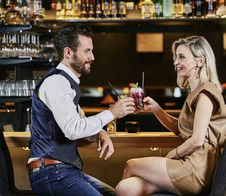 blonde Frau und Mann mit Bart prosten sich mit Cocktails an der Bar des Wellnesshotel Zum Bräu zu