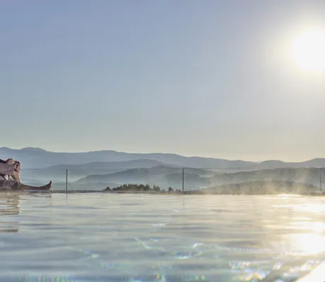 Paar in braunen Bademänteln sitzt am Beckenrand des Infinitypools im Wellnesshotel Zum Bräu im Abendrot